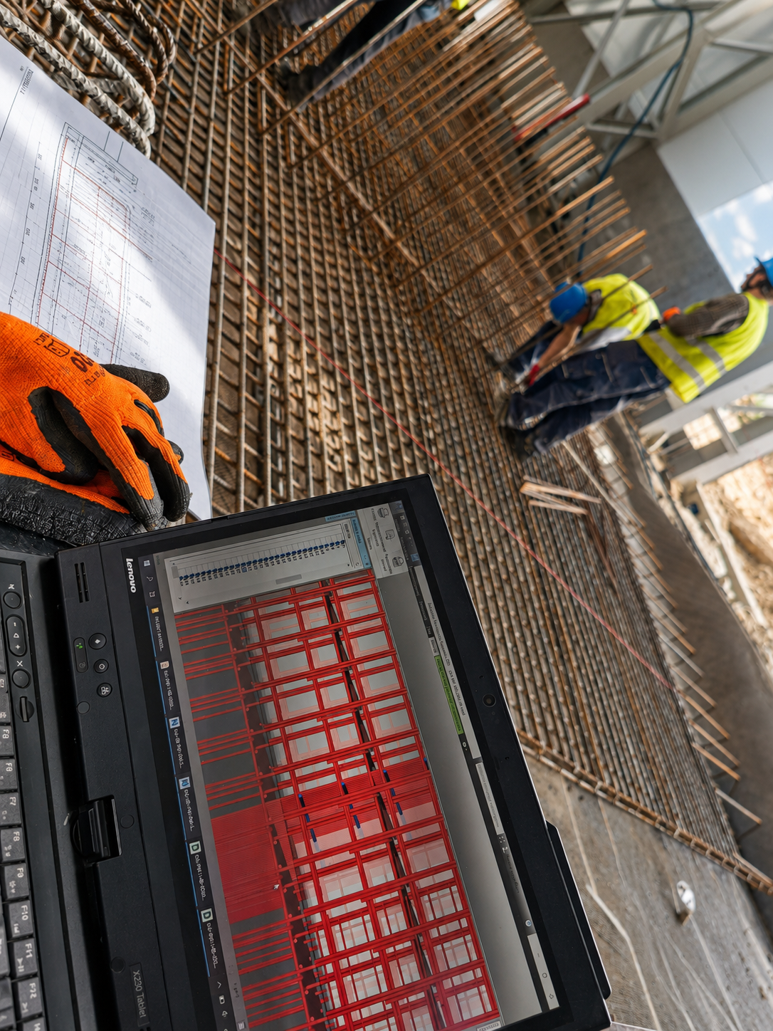 Rebar plan review on a tablet while a crew ties reinforcement